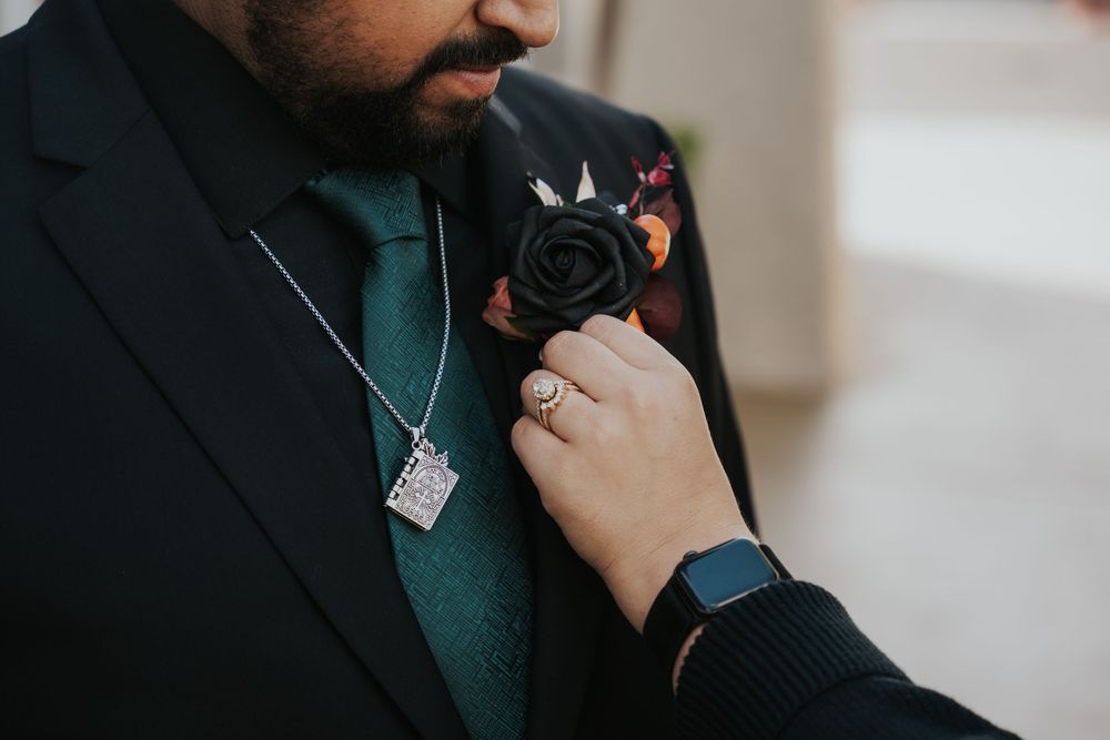 A person wearing a dark suit jacket adjusts their tie while wearing a teal colored shirt and smart watch.