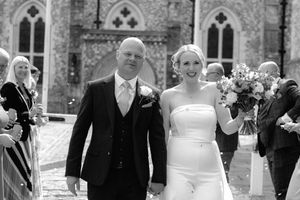 Wedding party members walk and pose outside a stone church building during a celebration.
