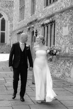 A black and white wedding photo series showing a couple walking together on a stone path next to a historic building.