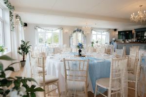 Elegant wedding reception venue with white chiavari chairs, crystal chandeliers, and soft blue accents throughout the space.