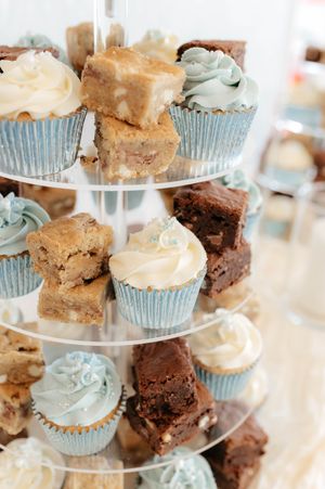 Tiered dessert display featuring chocolate brownies and cupcakes with blue frosting on an elegant white cake stand.