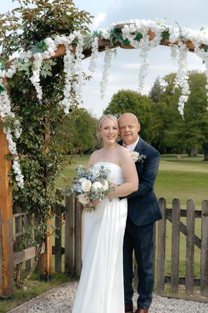 A couple shares romantic moments under a floral wedding arch on a golf course with white flowers and greenery.