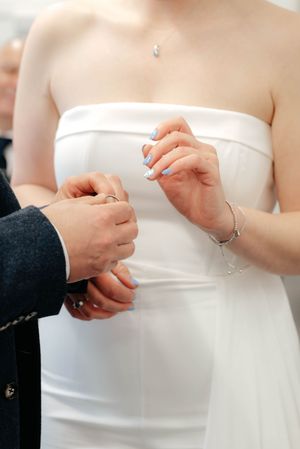 Close-up shot of hands exchanging wedding rings during a ceremony, with bride wearing white strapless dress.