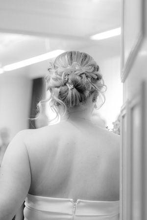 Black and white photo of an elegant updo hairstyle with delicate curls shown from multiple angles in a salon mirror.