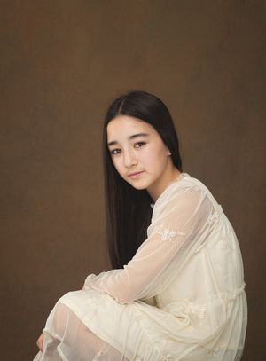 A woman in a flowing white dress poses gracefully against a dark brown background in a series of artistic portraits.