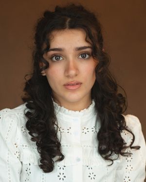 A person with dark curly hair and a white eyelet lace top poses in a series of four similar portraits.