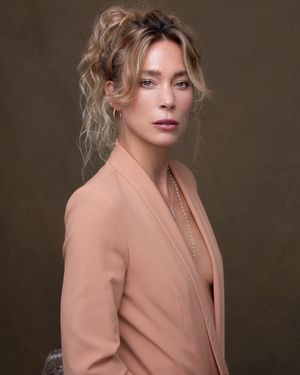 Fashion portrait with soft lighting features a person in a beige blazer against a dark brown studio backdrop.