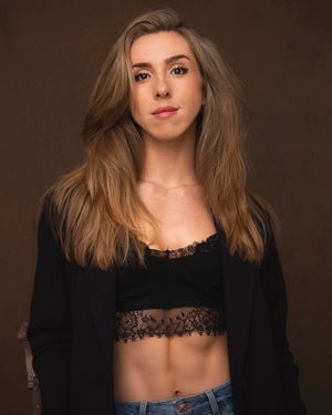 Studio portrait with dramatic lighting featuring a black blazer and lace top against a dark brown background.