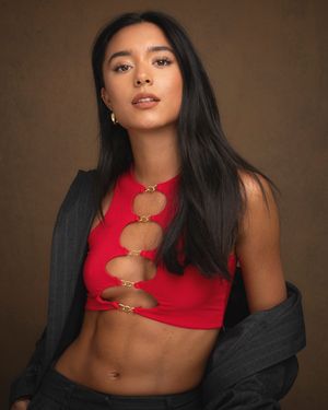 Fashion model in red crop top and black jacket poses against brown backdrop in glamour photoshoot series.