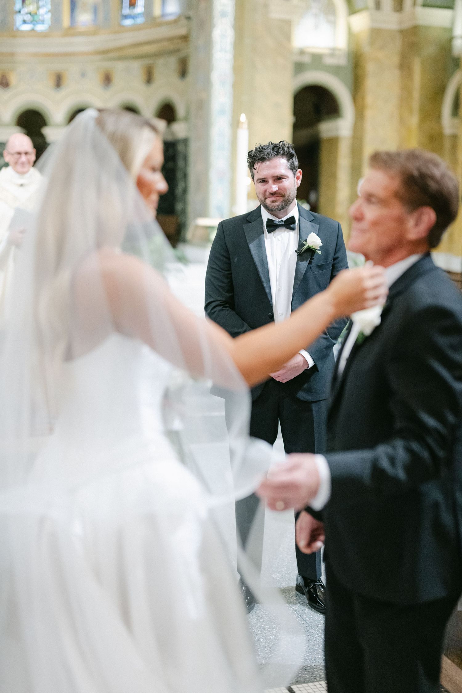 Wedding guests dance and celebrate in an elegant ballroom with ornate architectural details and large windows.