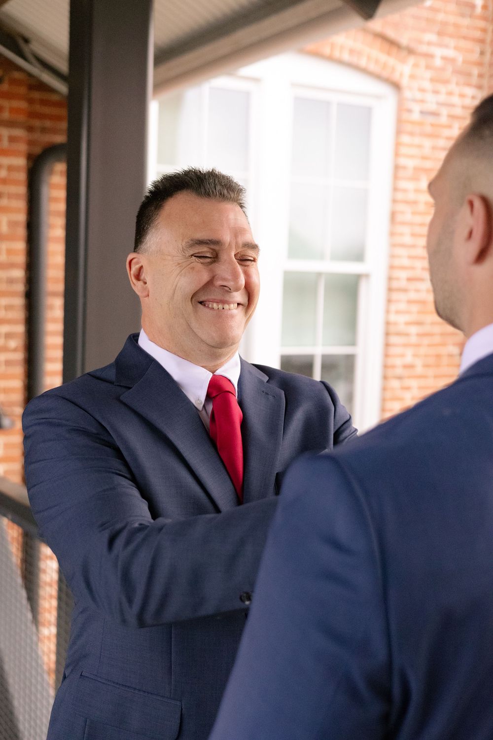 Groomsmen share a lighthearted moment together in navy suits and red ties before the wedding ceremony.