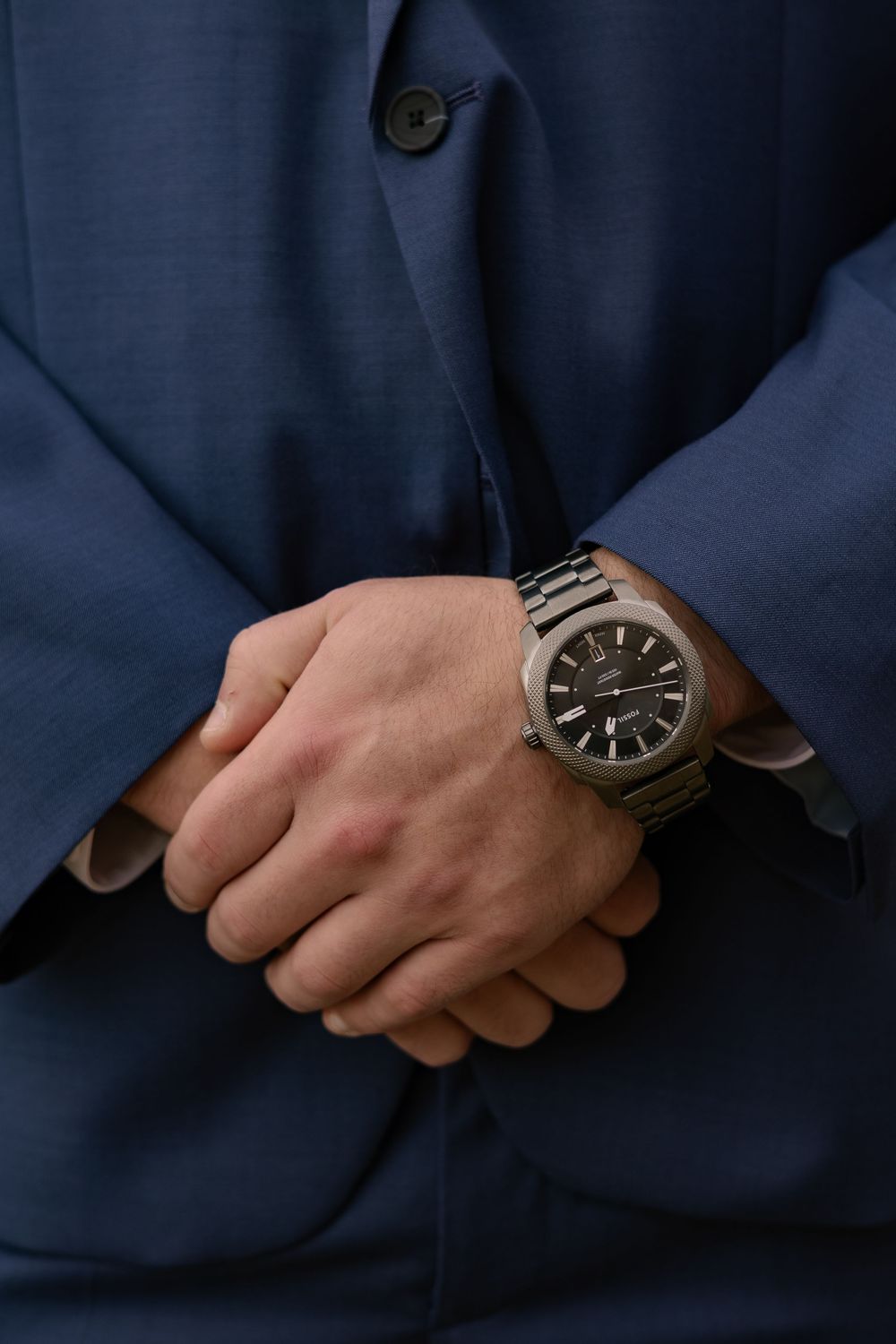 Close-up sequence of hands adjusting a sleek black wristwatch against a dark blue suit sleeve background.