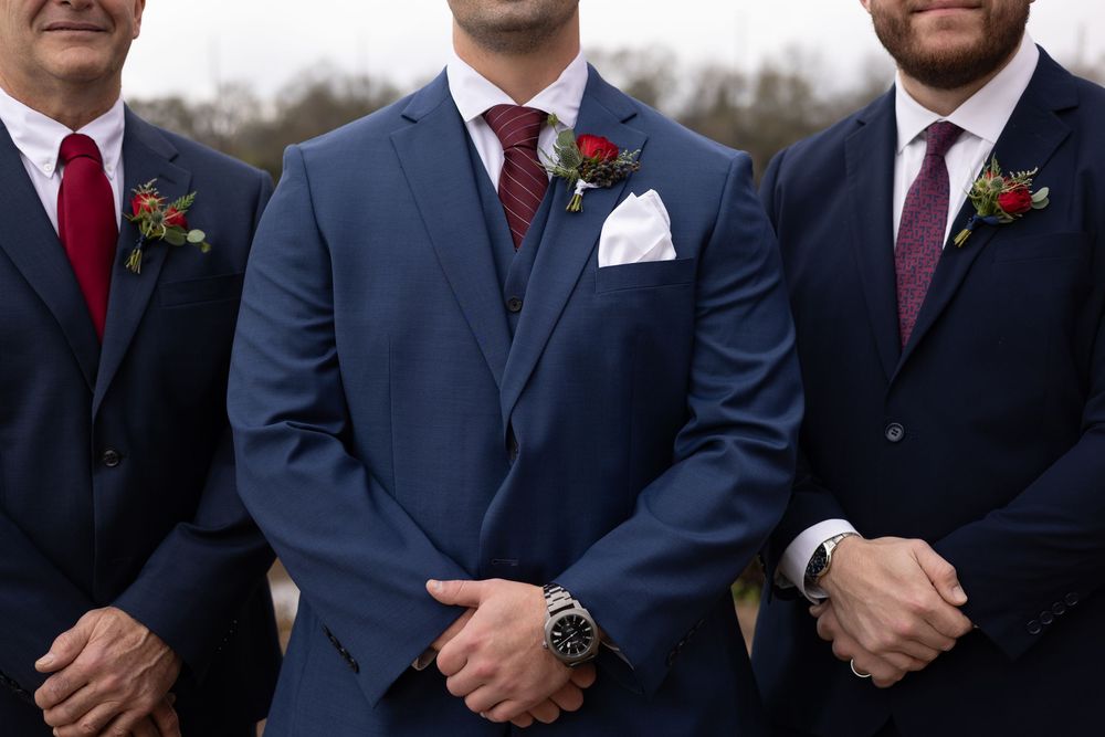 Groomsmen in coordinated suits with burgundy and red ties stand together at a formal wedding event.