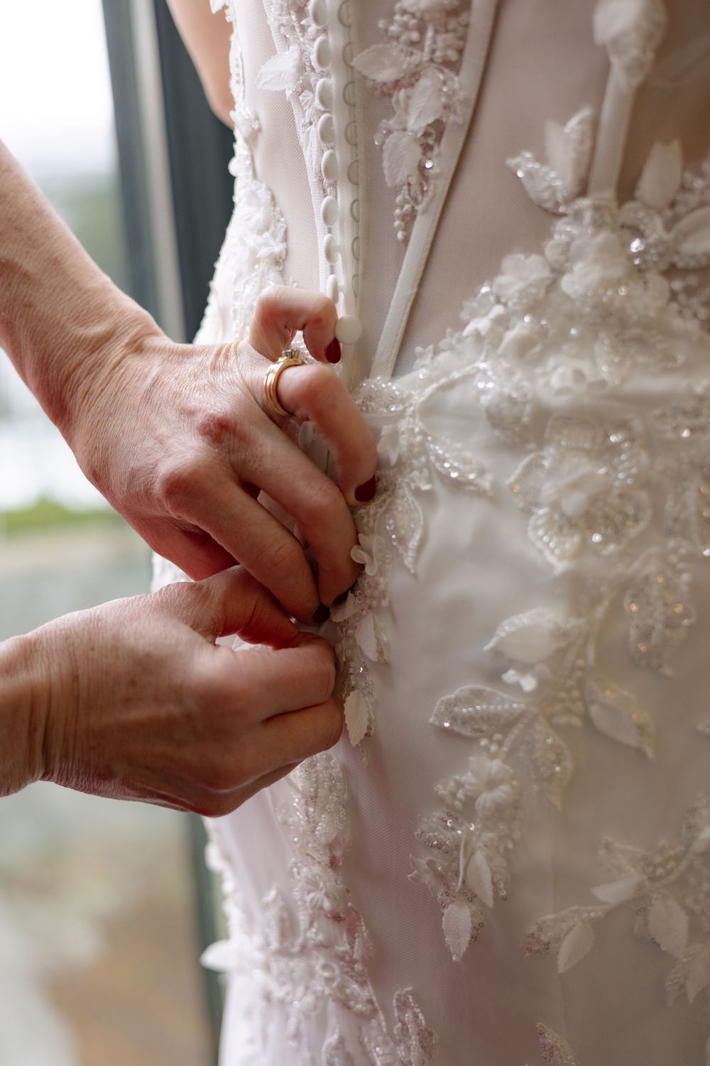 Close-up details of delicate lace and beading on a white wedding dress being adjusted.