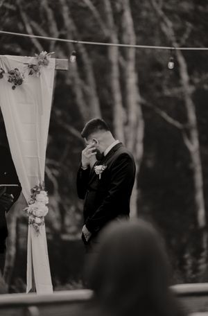 Black and white wedding ceremony photo showing white fabric draping and decorative elements outdoors.
