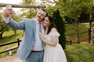 Bride and groom taking a selfie outdoors at their wedding venue, surrounded by lush greenery.