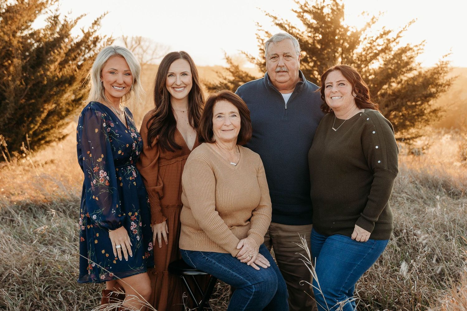 A group of people pose together outdoors at sunset with golden light filtering through autumn foliage.