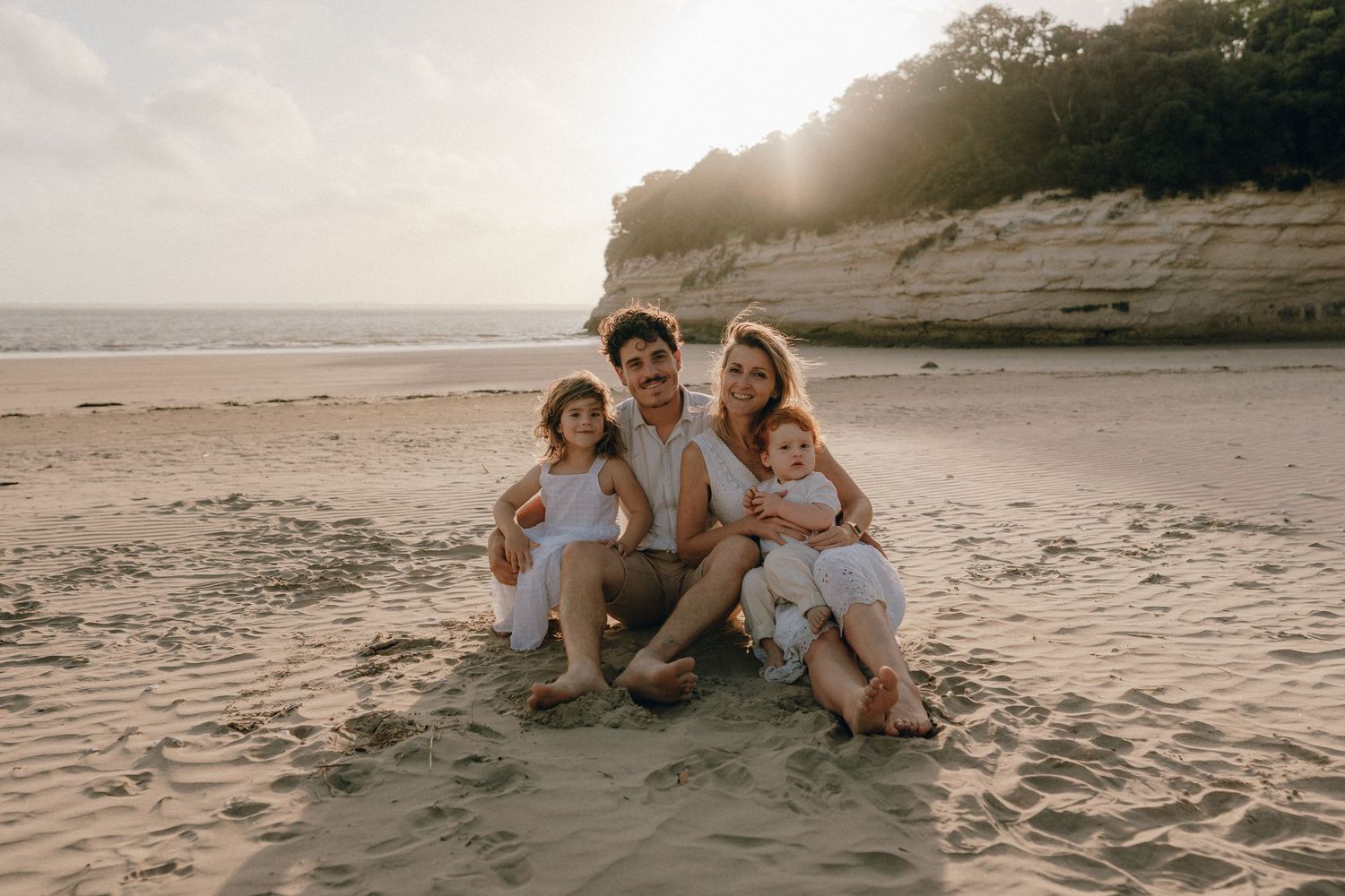 Photo famille posée sur le sable, en contre-jour face au soleil.