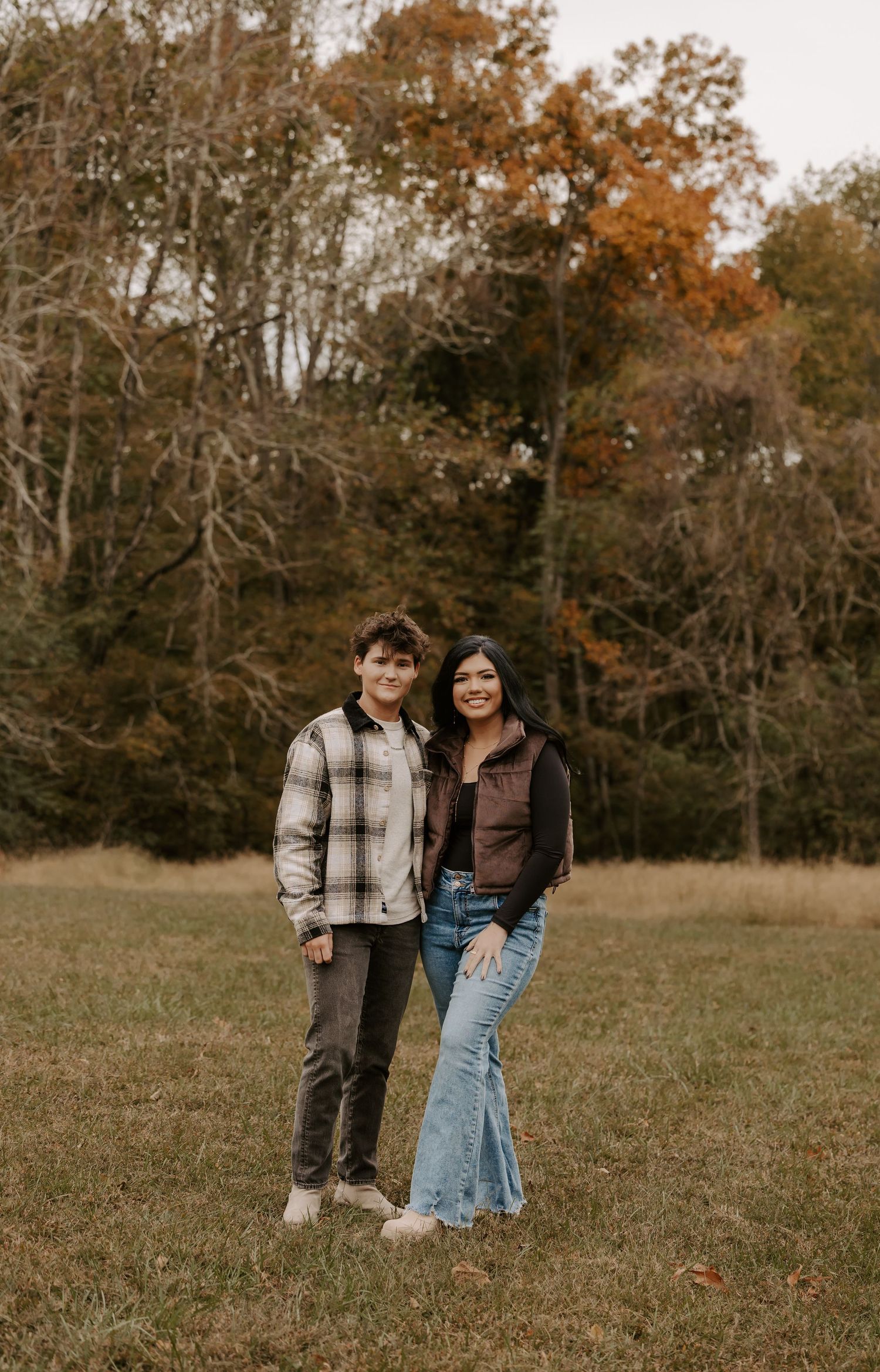 Couple standing together in an autumn field with golden foliage in the background.