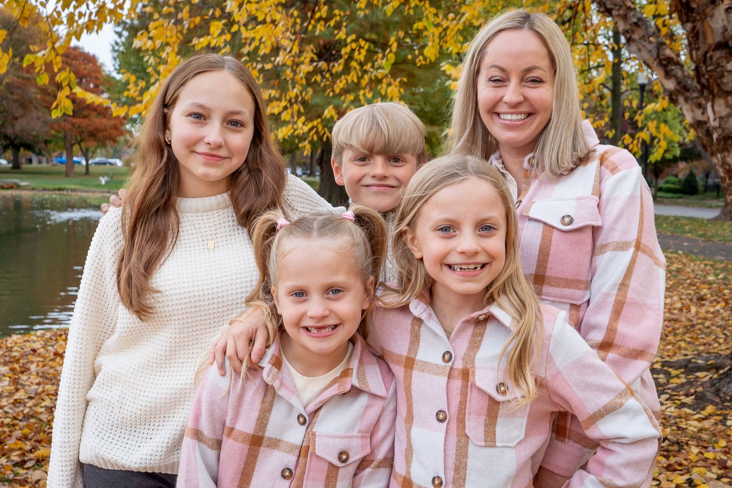 A group wearing coordinated pink and white outfits poses together against a backdrop of autumn trees with golden leaves.
