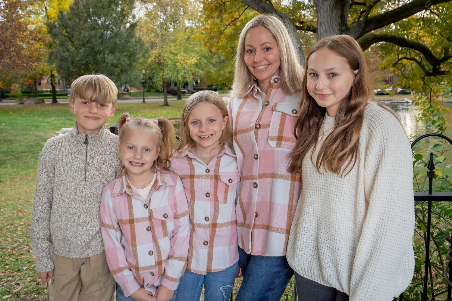 A group wearing coordinated pink and white outfits poses together for outdoor autumn family photos in a park setting.