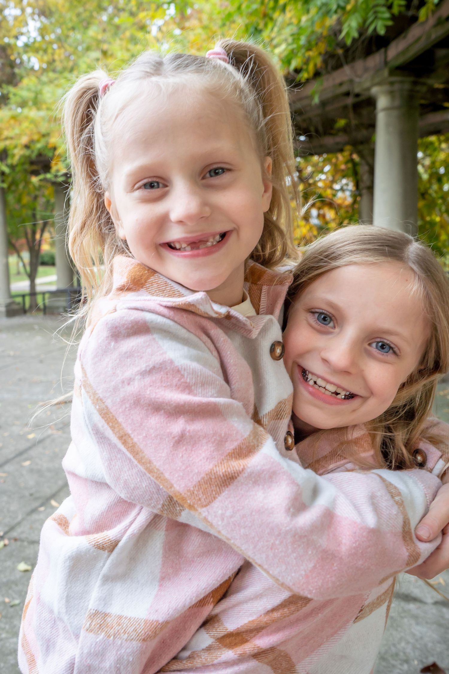 Two children share a joyful embrace while wearing matching pink sweaters outdoors in autumn.