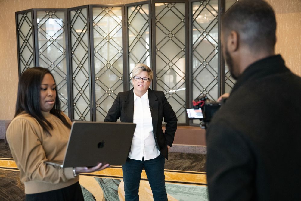 A group of people having an animated discussion in a business office setting with glass partitions visible.