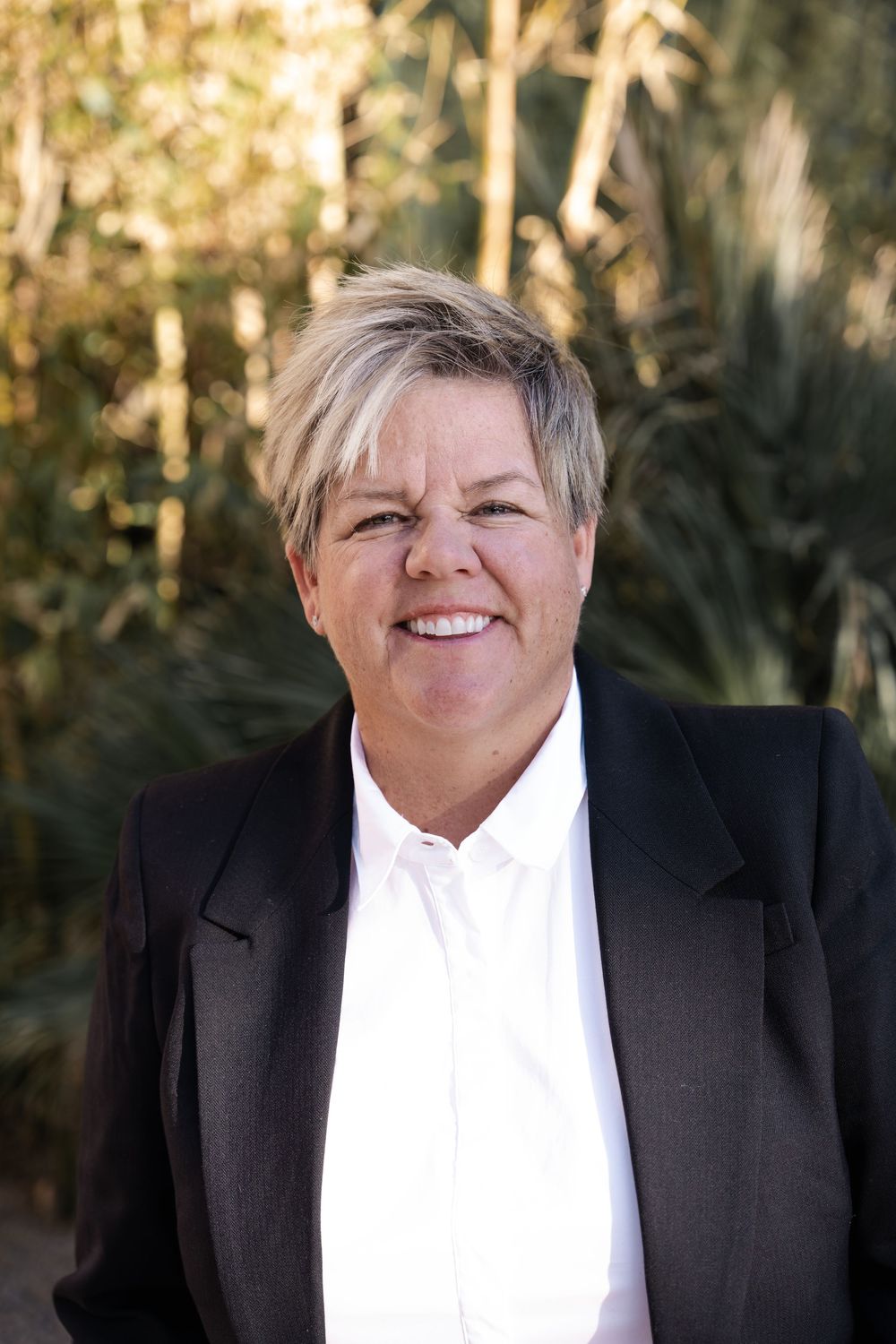 Professional headshot series showing four similar poses in a black suit and white shirt against a natural background.