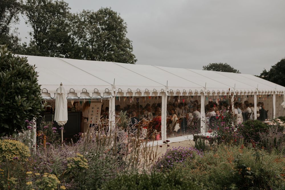Exterior view of a large white wedding marquee surrounded by lavender gardens on an overcast day.