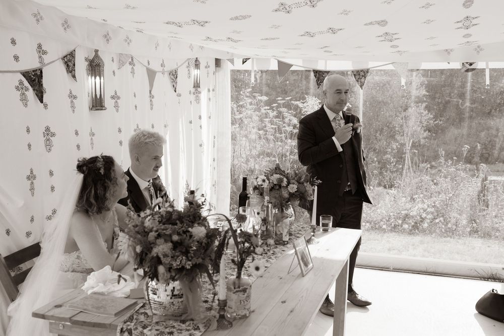 Black and white photo of a man giving a wedding speech at an elegantly decorated reception table.