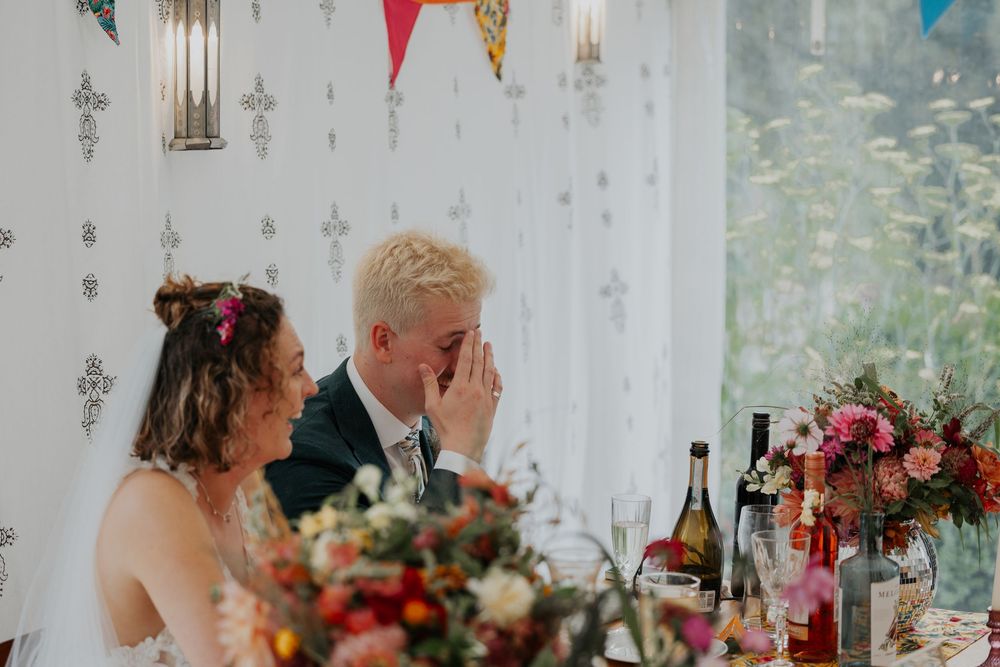 Bride and groom share a laugh at the wedding reception table decorated with colorful bunting.
