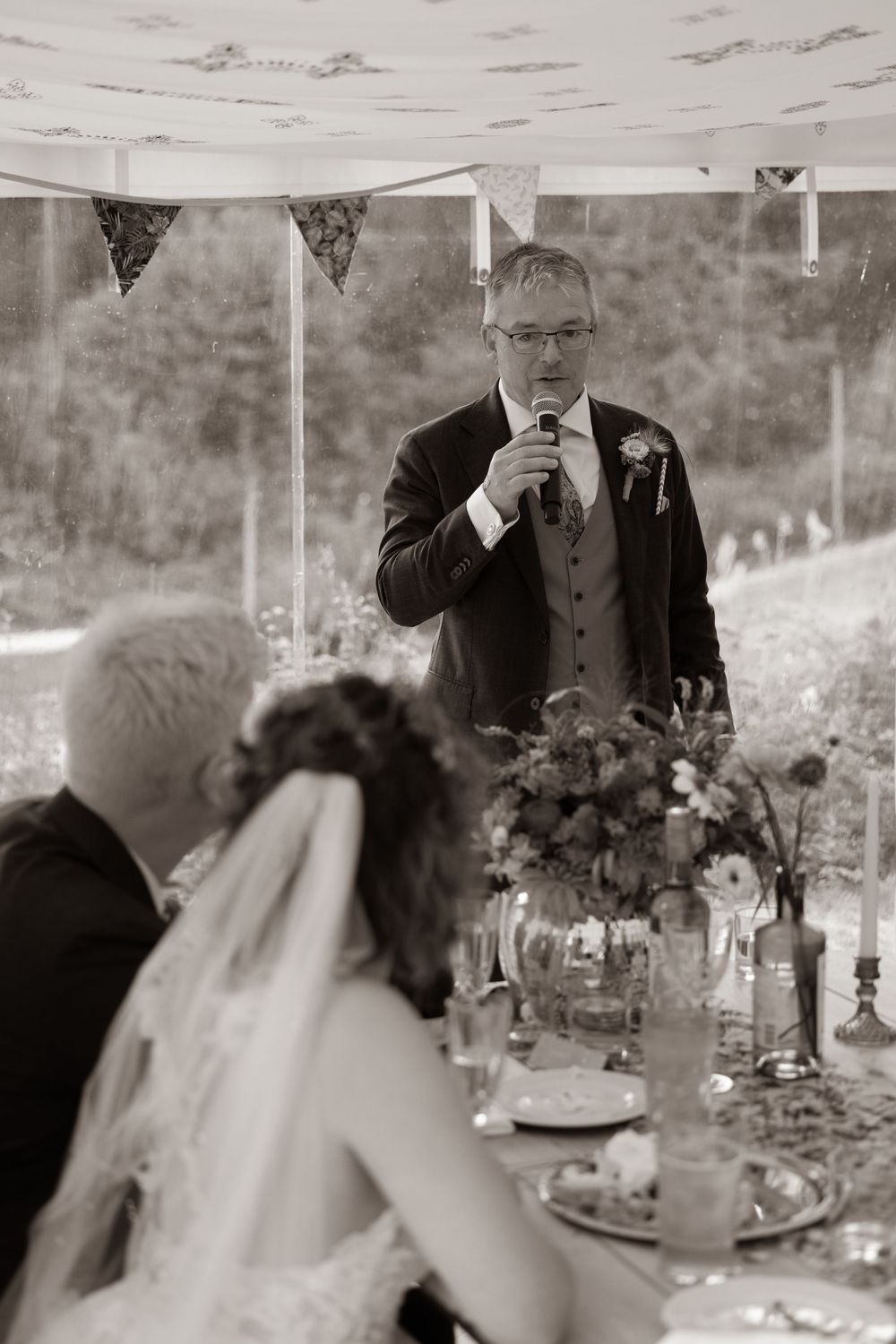 Black and white photo of a man giving a heartfelt wedding speech at a beautifully set reception table.