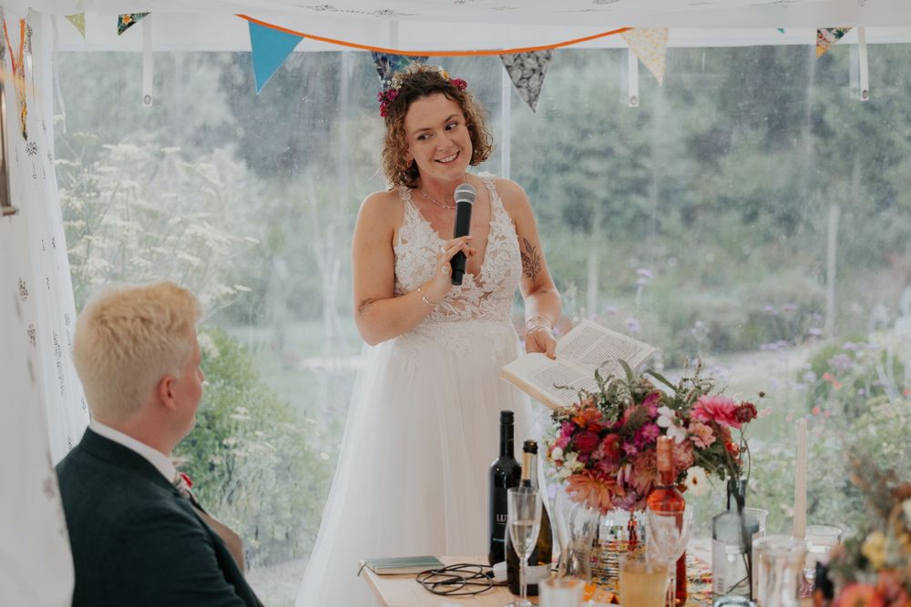 Smiling bride delivers her wedding speech holding a microphone at the decorated reception table.