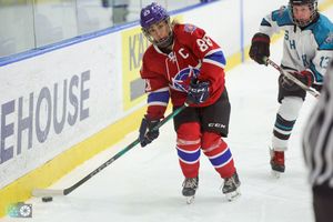 Hockey players in red and teal jerseys chase after the puck during an intense game on the ice.