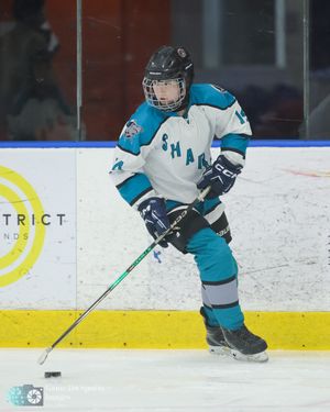 Youth hockey player in teal jersey skates with puck during practice session on indoor ice rink.