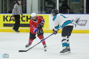 Youth hockey players in red and teal jerseys compete for the puck during an ice hockey game.