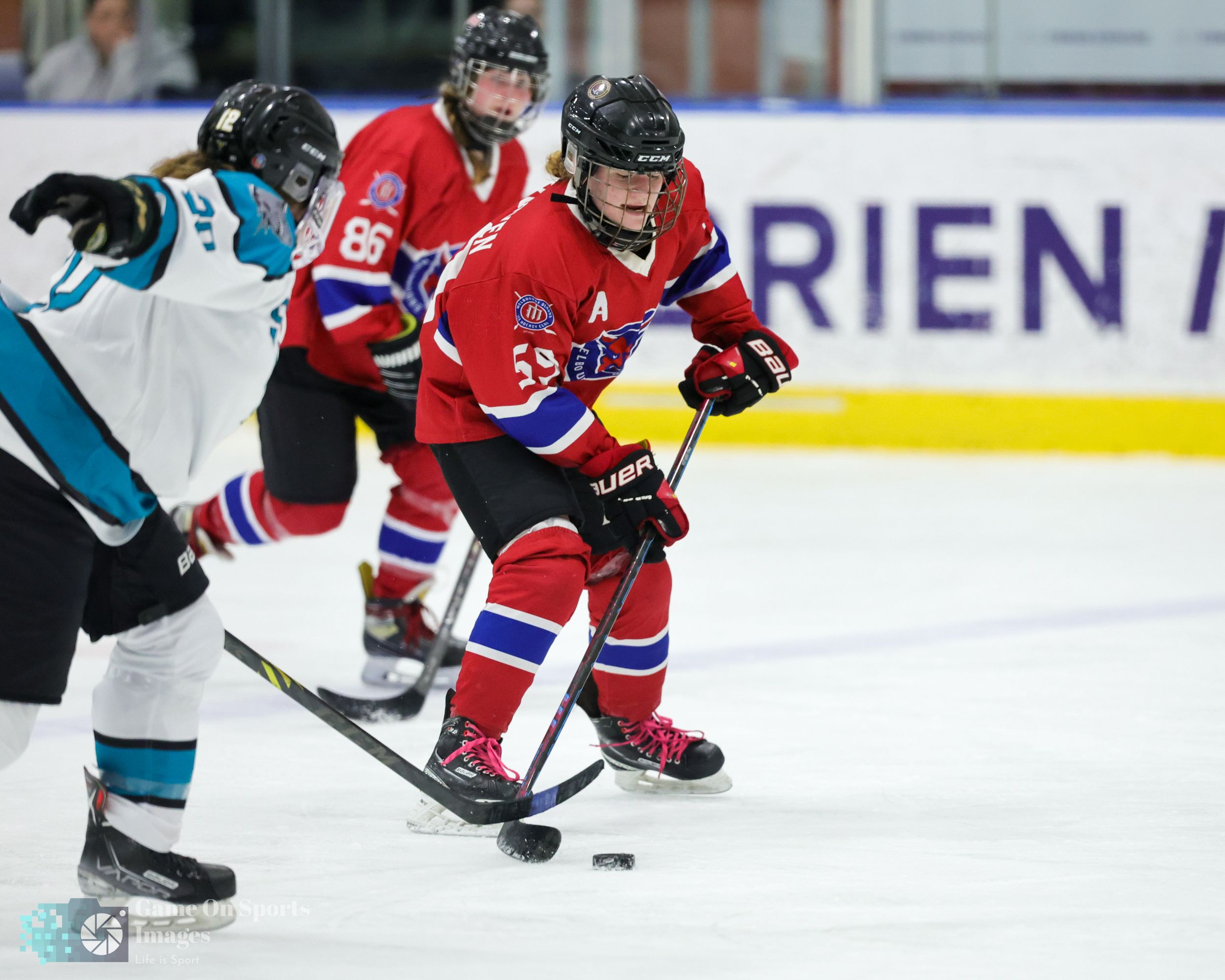 Hockey players battle for control of the puck during an intense game between teams in red and teal jerseys.