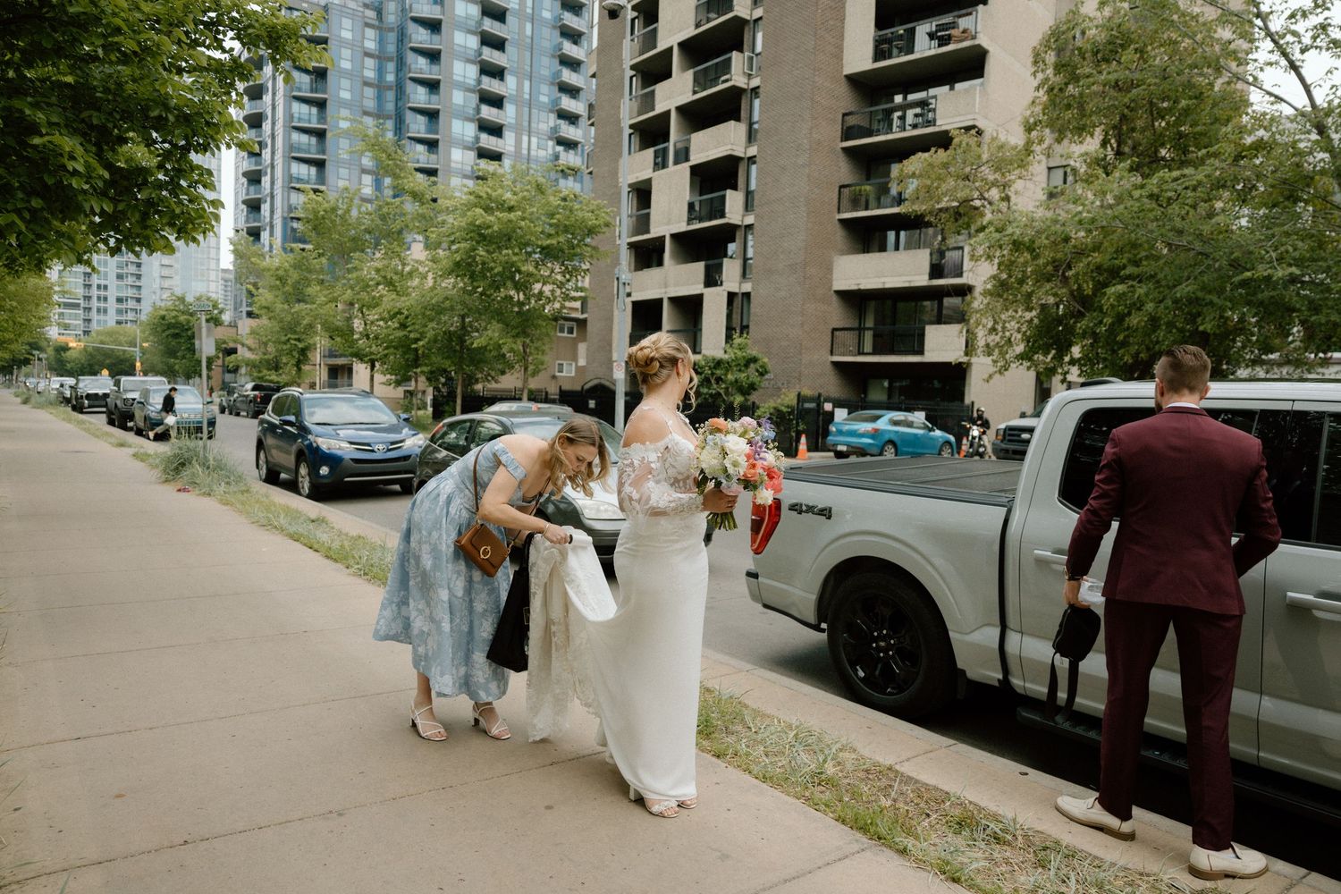 A group walks down a tree-lined urban sidewalk with tall apartment buildings in the background.