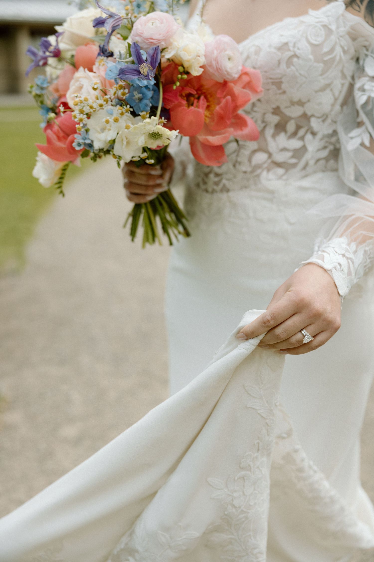 Close-up of a white lace wedding dress with colorful floral bouquet featuring pink and peach blooms.