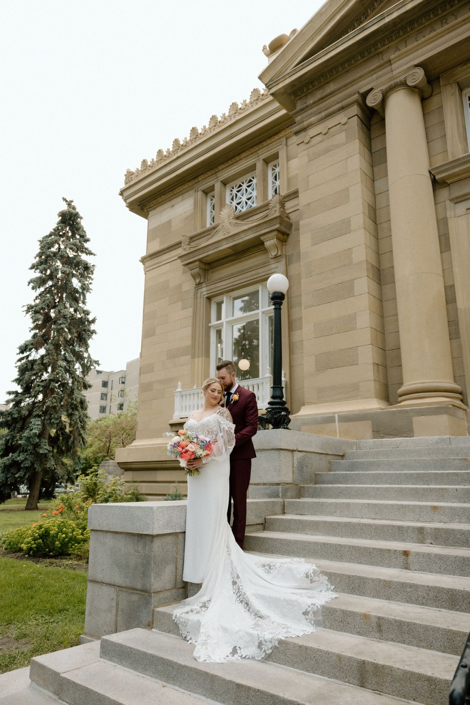 A wedding couple poses on grand stone steps of a historic building with elegant architecture.