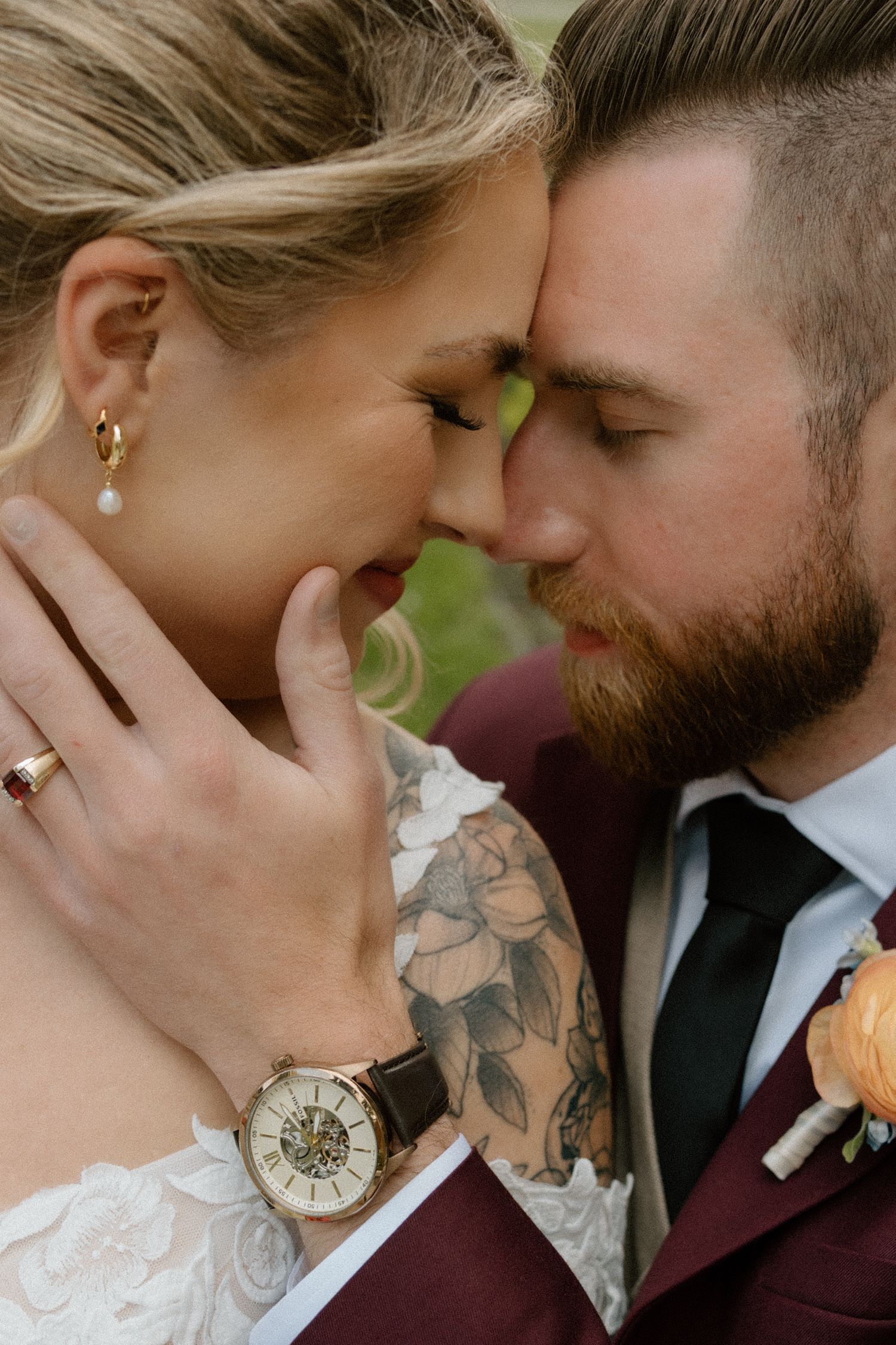 Intimate close-up wedding portrait with burgundy suit details and floral boutonniere.