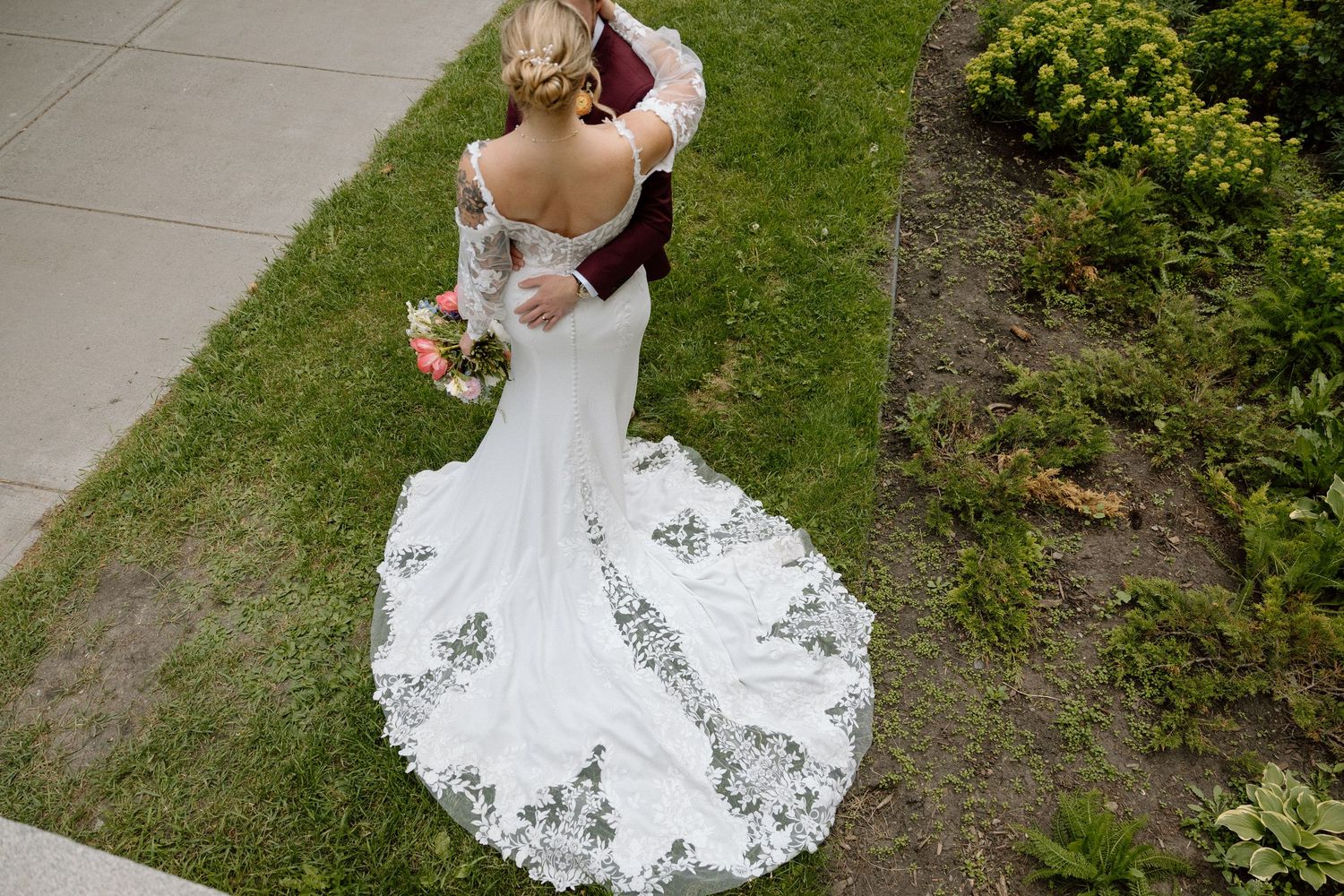 Overhead view of a bride's lace-trimmed wedding dress train on grass.