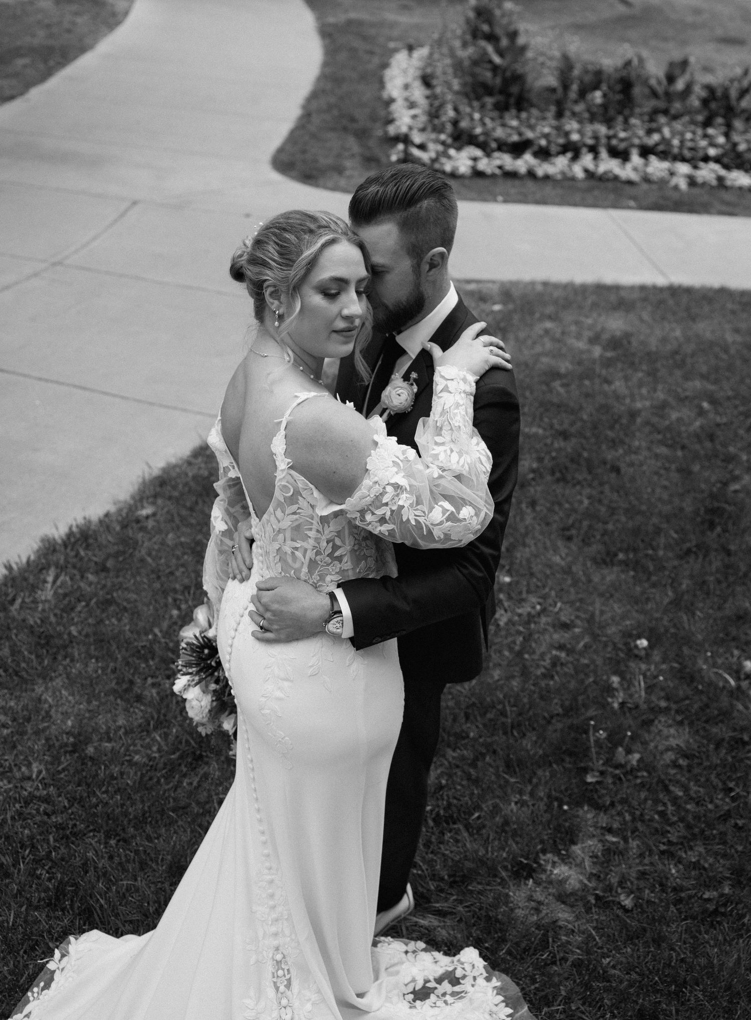 Black and white portrait of wedding couple embracing on garden path.