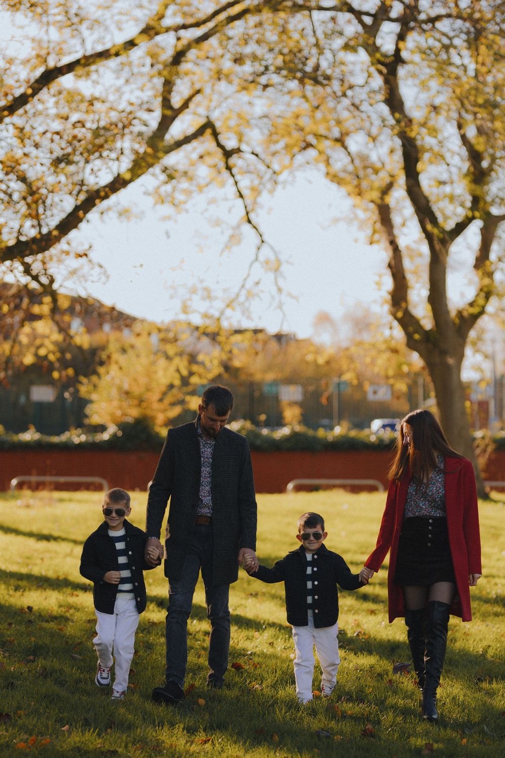 Family walking together in a park during golden hour autumn sunlight with fallen leaves on the ground.