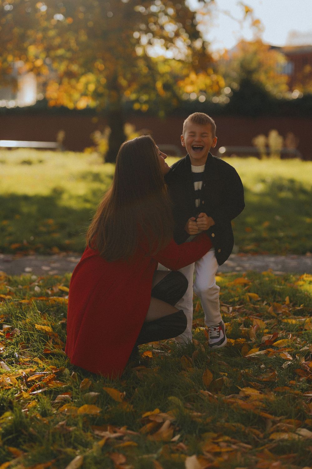 A couple sits together among fallen autumn leaves on the ground during a sunny fall afternoon.