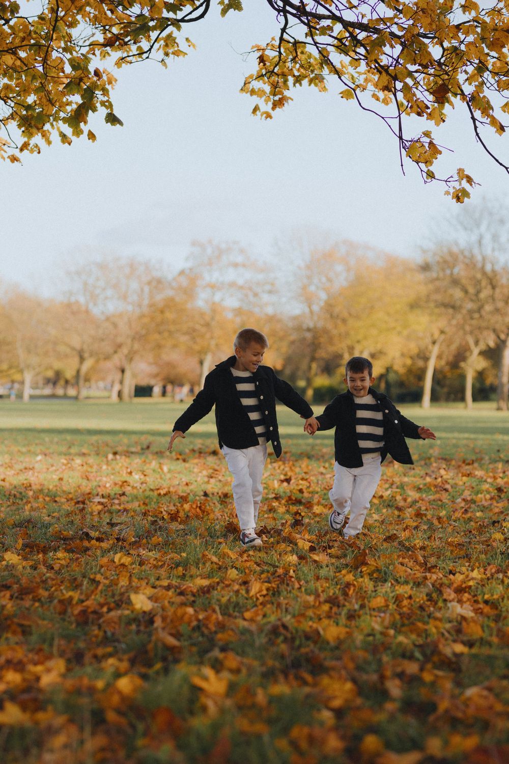 Children playing in a blanket of orange and brown fallen leaves during autumn.