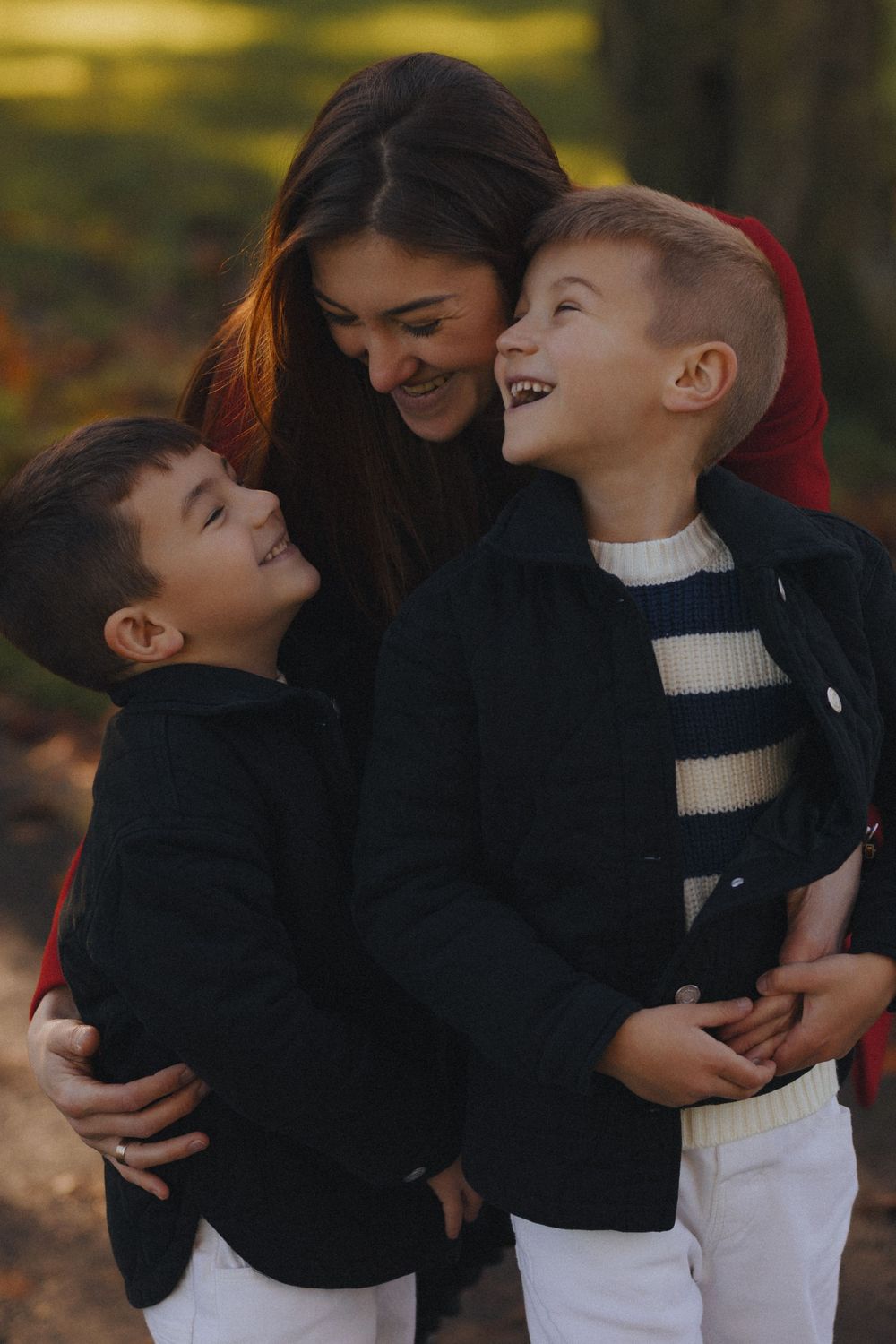 A family embraces and laughs together outdoors during a playful autumn photoshoot.