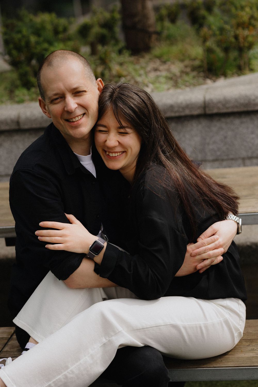 Two people in black and white outfits share an intimate embrace while sitting outdoors.