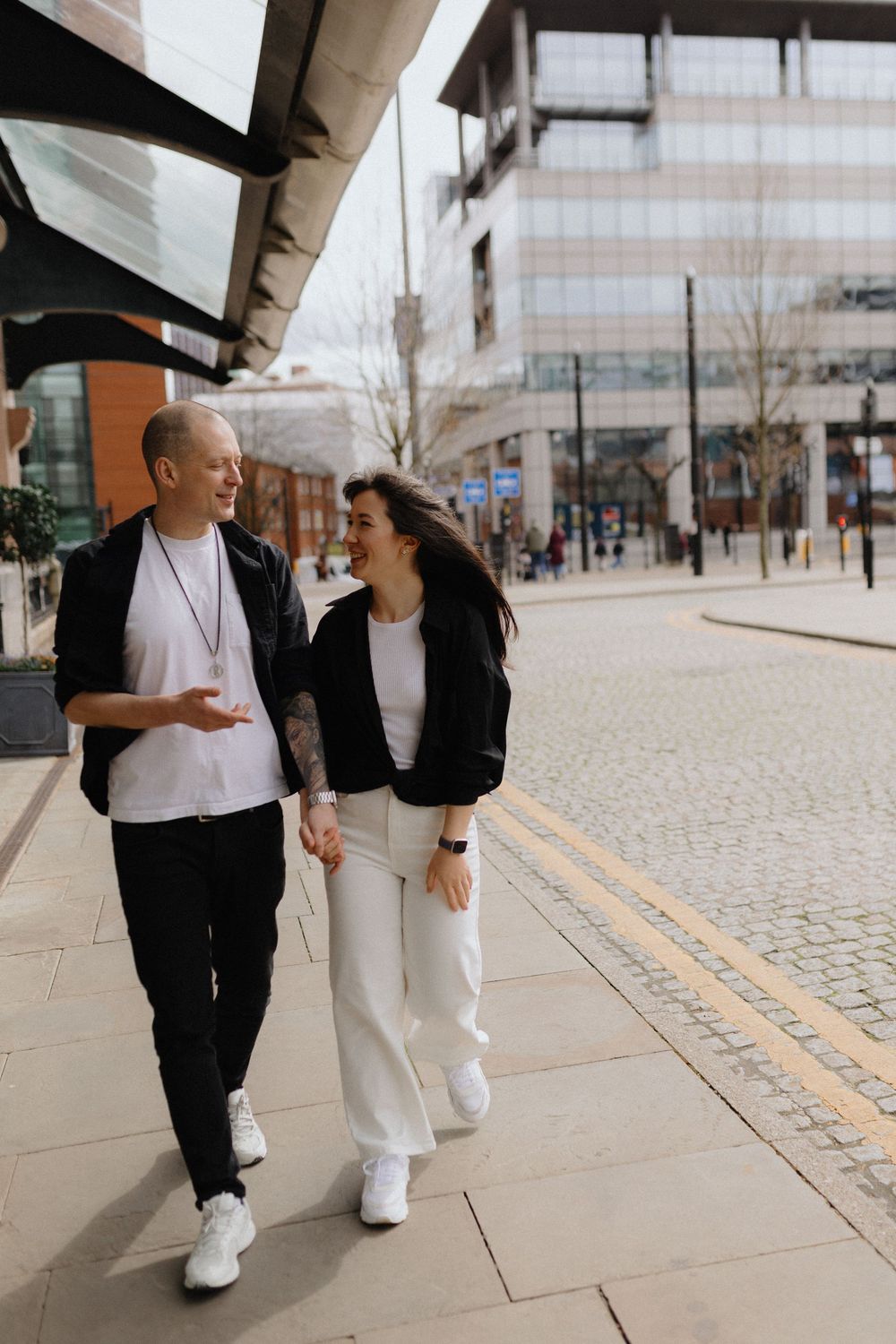 A couple strolls together on a modern cobblestone walkway wearing contrasting black and white outfits.