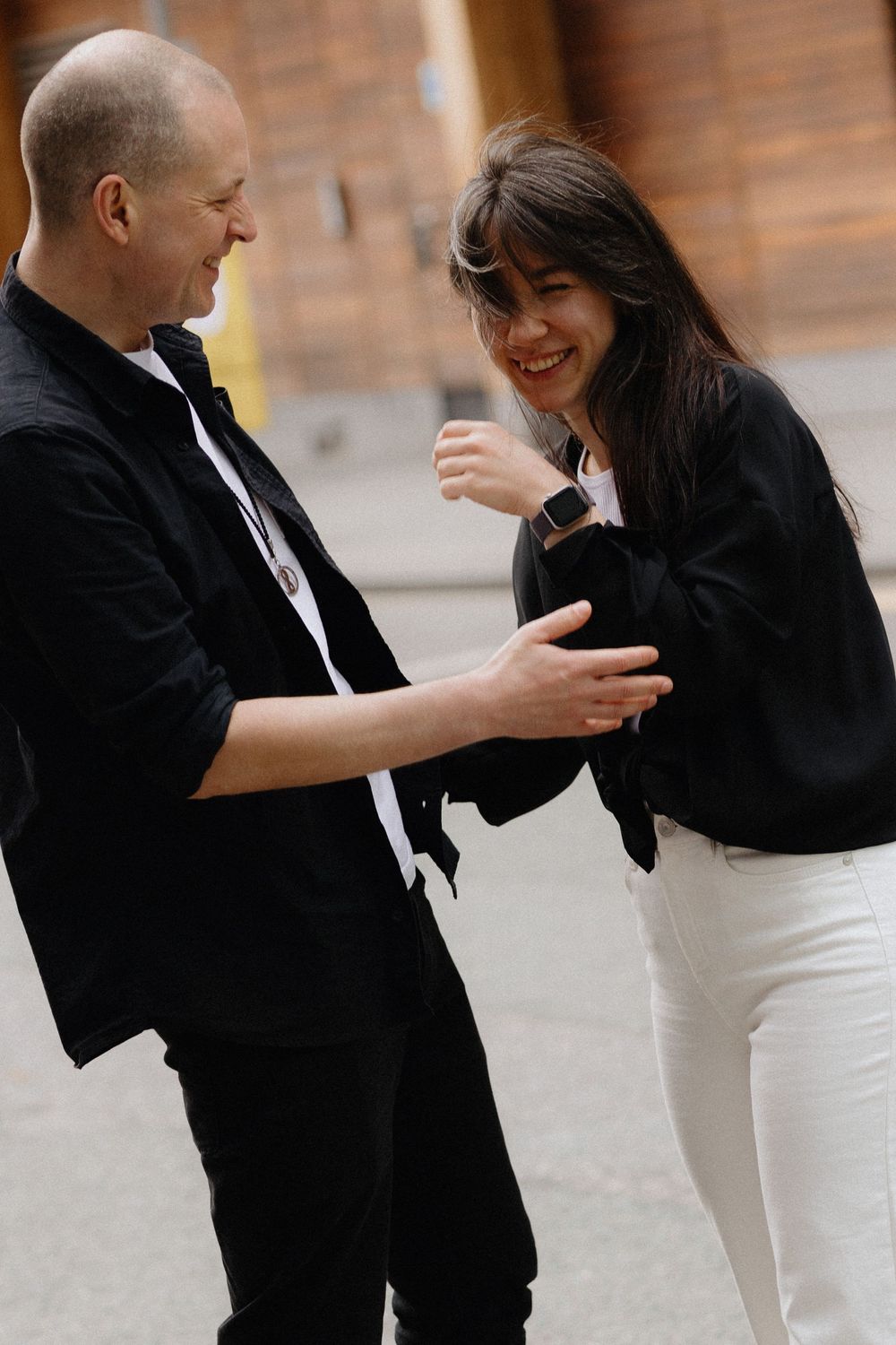 A couple in formal attire sharing a candid moment while dancing together against a brick wall background.